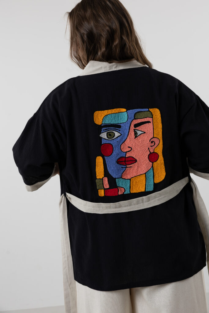 Artisanal abstract face embroidered muslin wrap kimono; unisex line-art cotton duster for sustainable resort wear, travel, and modern bohemian style.
