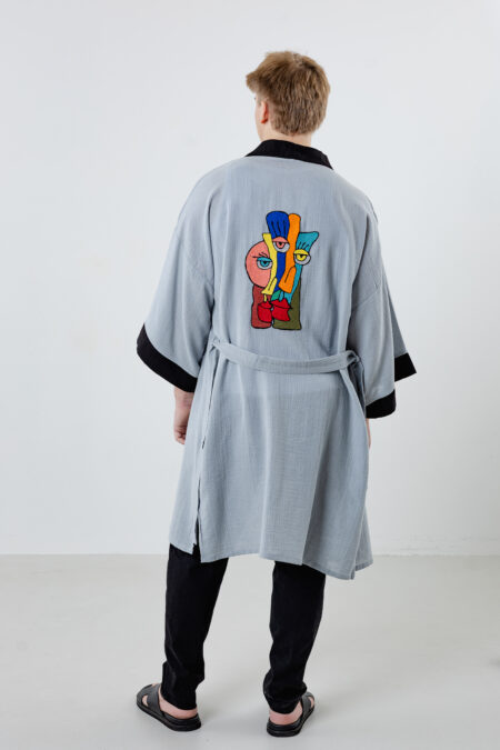 Artisanal abstract face embroidered muslin wrap kimono; unisex line-art cotton duster for sustainable resort wear, travel, and modern bohemian style.