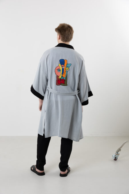 Artisanal abstract face embroidered muslin wrap kimono; unisex line-art cotton duster for sustainable resort wear, travel, and modern bohemian style.