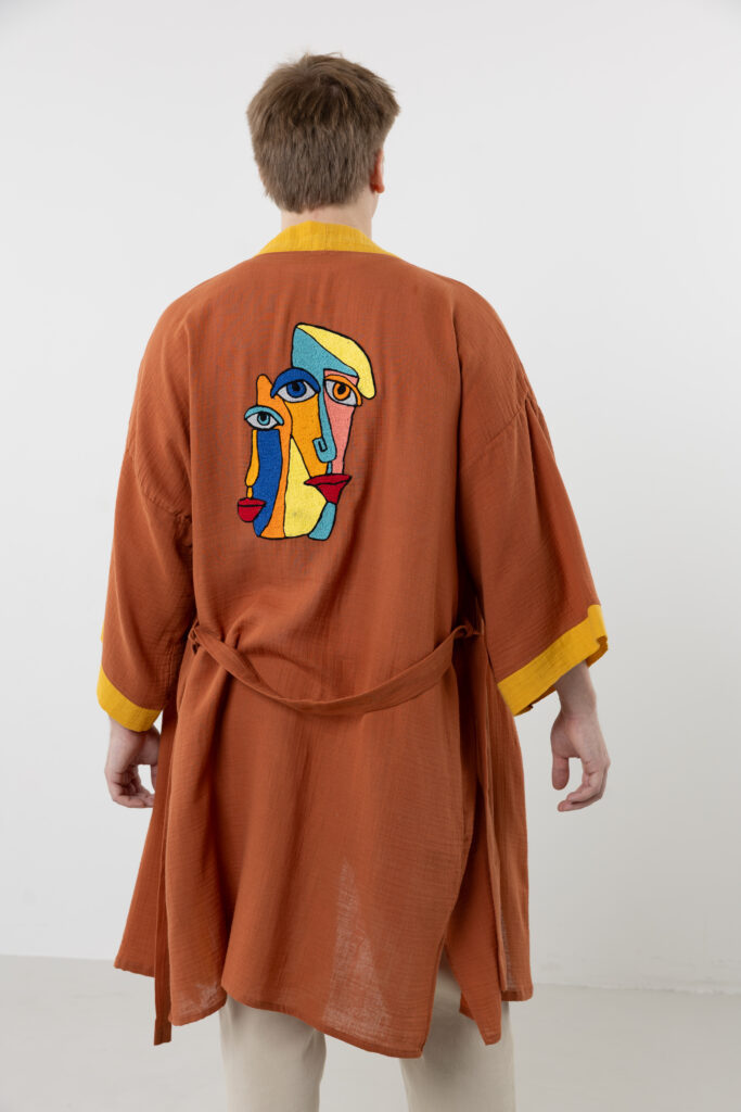 Artisanal abstract face embroidered muslin wrap kimono; unisex line-art cotton duster for sustainable resort wear, travel, and modern bohemian style.