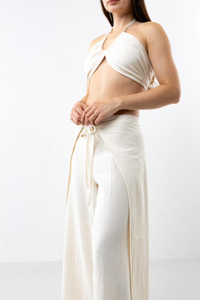 Artisanal natural cotton double-tie wrap pants; adjustable cream open-side trousers with front and back ties for sustainable resort wear and minimalist travel style.