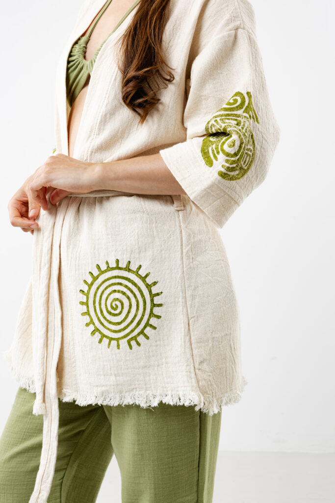 Short artisanal cotton kimono in natural cream with green woodblock spiral patterns.