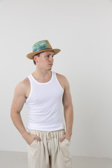 Man wearing a hand-painted sailing straw fedora on a boat or beach.